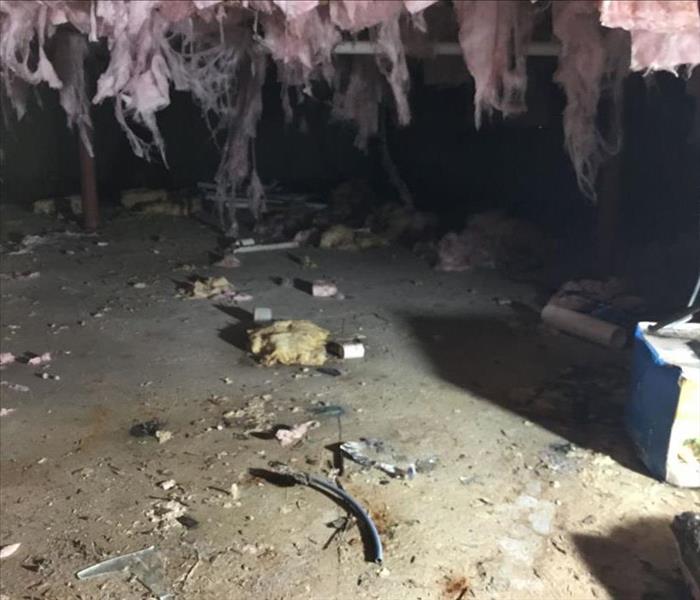 Heavily damaged crawlspace with debris and hanging, tattered insulation